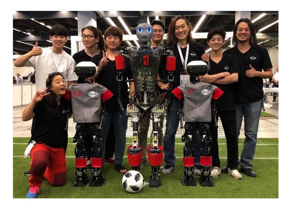 Fig. 1. The members of Team HERoEHS with their robot 'ALICE's (sides) and Team Sweaty's robot (center) at Robocup 2018