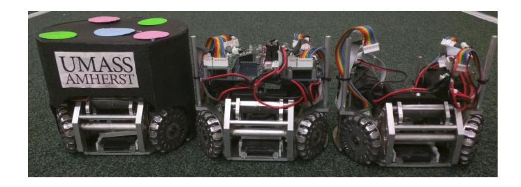 Fig. 1: Completed SSL Robots. The robot in the center showcases the modular electronics. The large blue circuit board is the main board. The purple board is the kicker driver. The green boards are the motor drivers. The robot on the right has had the electronics removed for a better view of the drive system.